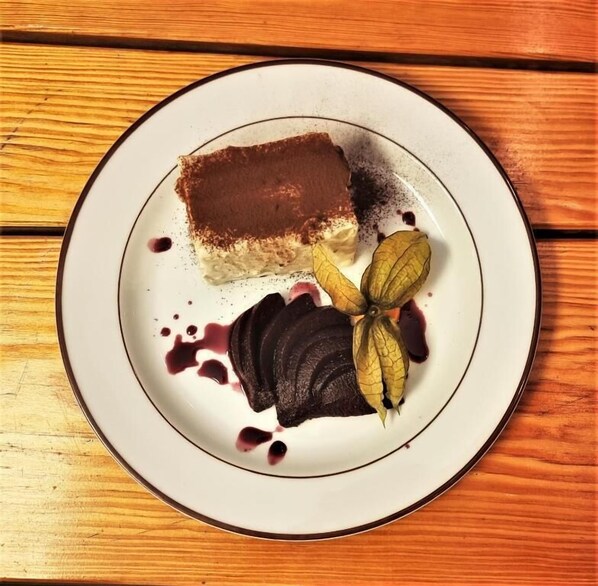 A dessert plate with a slice of cake, a fruit arrangement, and a dollop of cream on a wooden table. - Waldhotel am See Berlin-Schmöckwitz (Berlin)