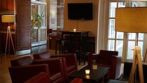 Une pièce chaleureuse avec des canapés en cuir rouge, une petite table avec une bougie, un téléviseur fixé au mur et une grande fenêtre avec des stores.