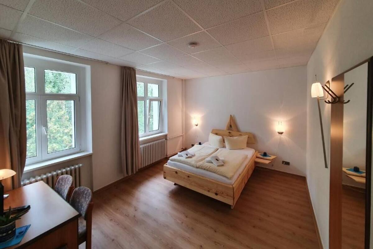 Une chambre à coucher avec un lit en bois, un bureau et une chaise, une fenêtre avec des rideaux et une lampe fixée au mur.