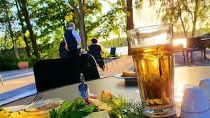 Une table à manger avec une assiette de nourriture, un verre de bière et, en arrière-plan, des personnes.