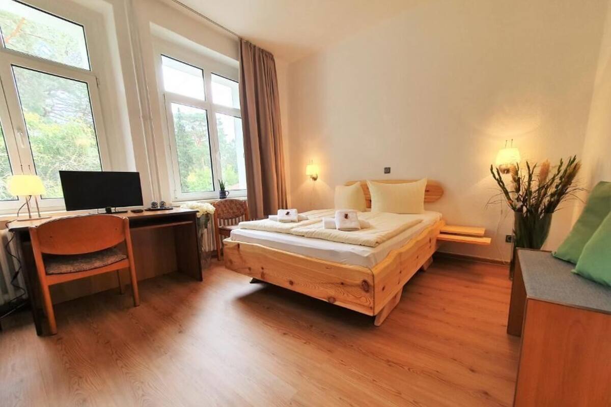 Une chambre à coucher avec un lit en bois, un bureau avec un ordinateur et de grandes fenêtres.
