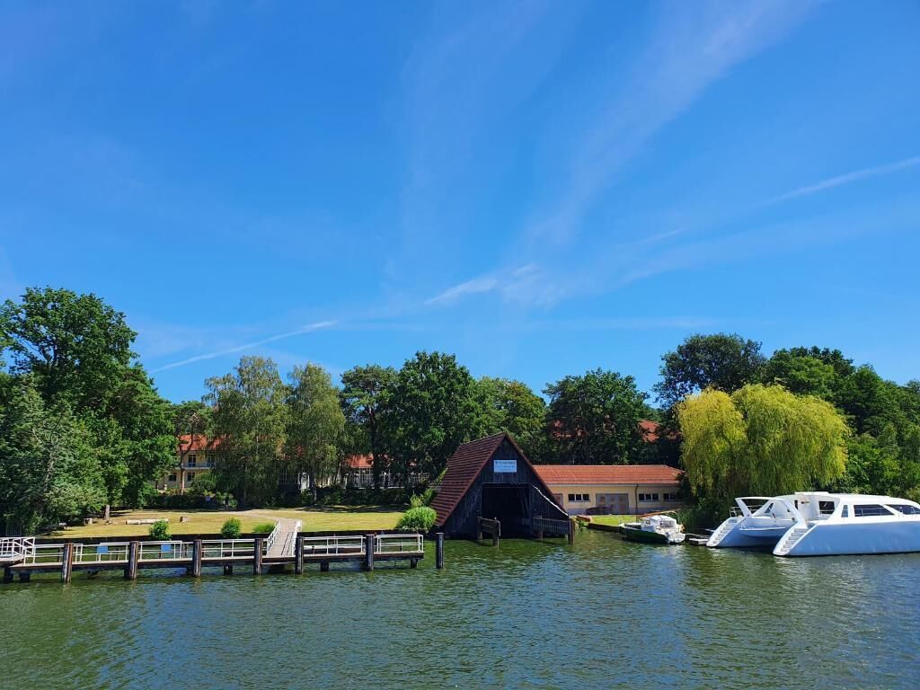 A dock with a covered boat house, a white yacht, and a building with a red roof in a lakeside setting.