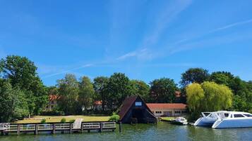 A dock with a covered boat house, a white yacht, and a building with a red roof in a lakeside setting.