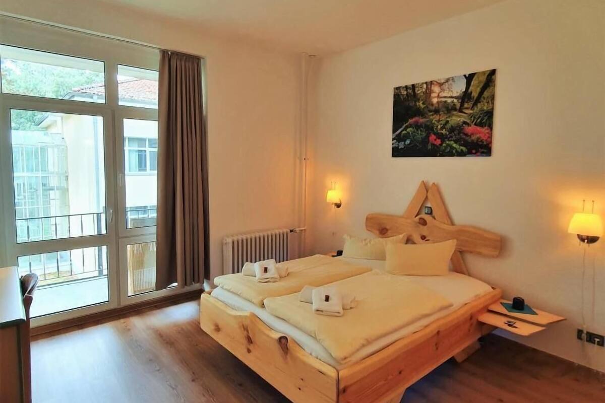 Un lit double avec une tête de lit en bois, deux tables de chevet, un radiateur et une fenêtre avec des rideaux.