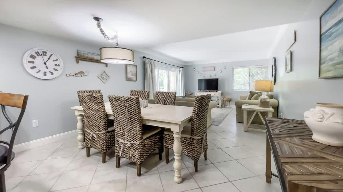 A dining area with a round table and chairs, a television in the background, and a sofa in the adjacent living room.
