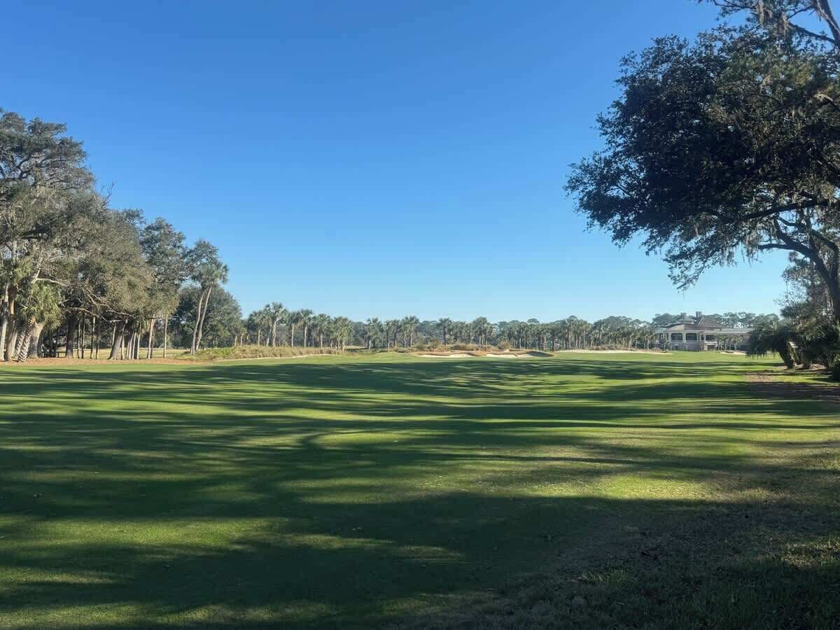 Un terrain de golf avec un ciel dégagé, des arbres et un bâtiment situé au loin.