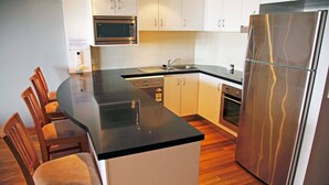 Une cuisine moderne avec un plan de travail noir, des appareils en acier inoxydable et des chaises en bois.
