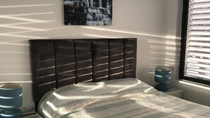 Une chambre à coucher comprenant un lit, une table de chevet, une fenêtre avec des stores et un tableau représentant une cascade, accroché au mur.