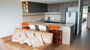 Une cuisine moderne avec un îlot central, des meubles de couleur sombre et un réfrigérateur.