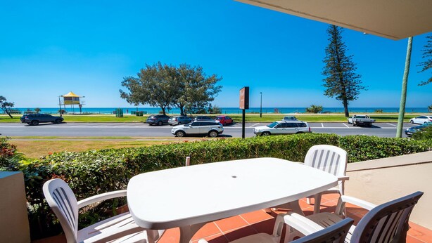 Eine Terrasse mit Tisch und Stühlen, die auf eine Straße mit Autos und Meerblick blickt.