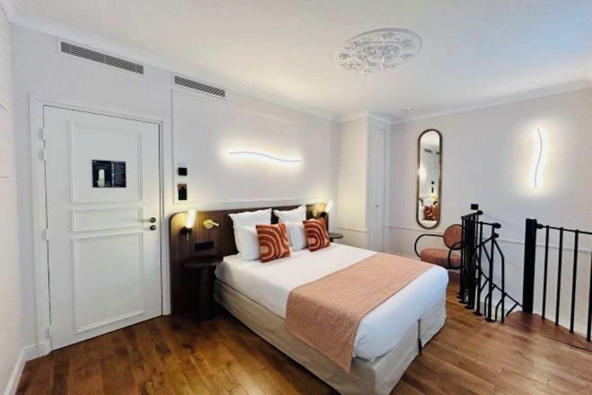 A hotel room with a bed, bedside tables, a mirror, and a door.