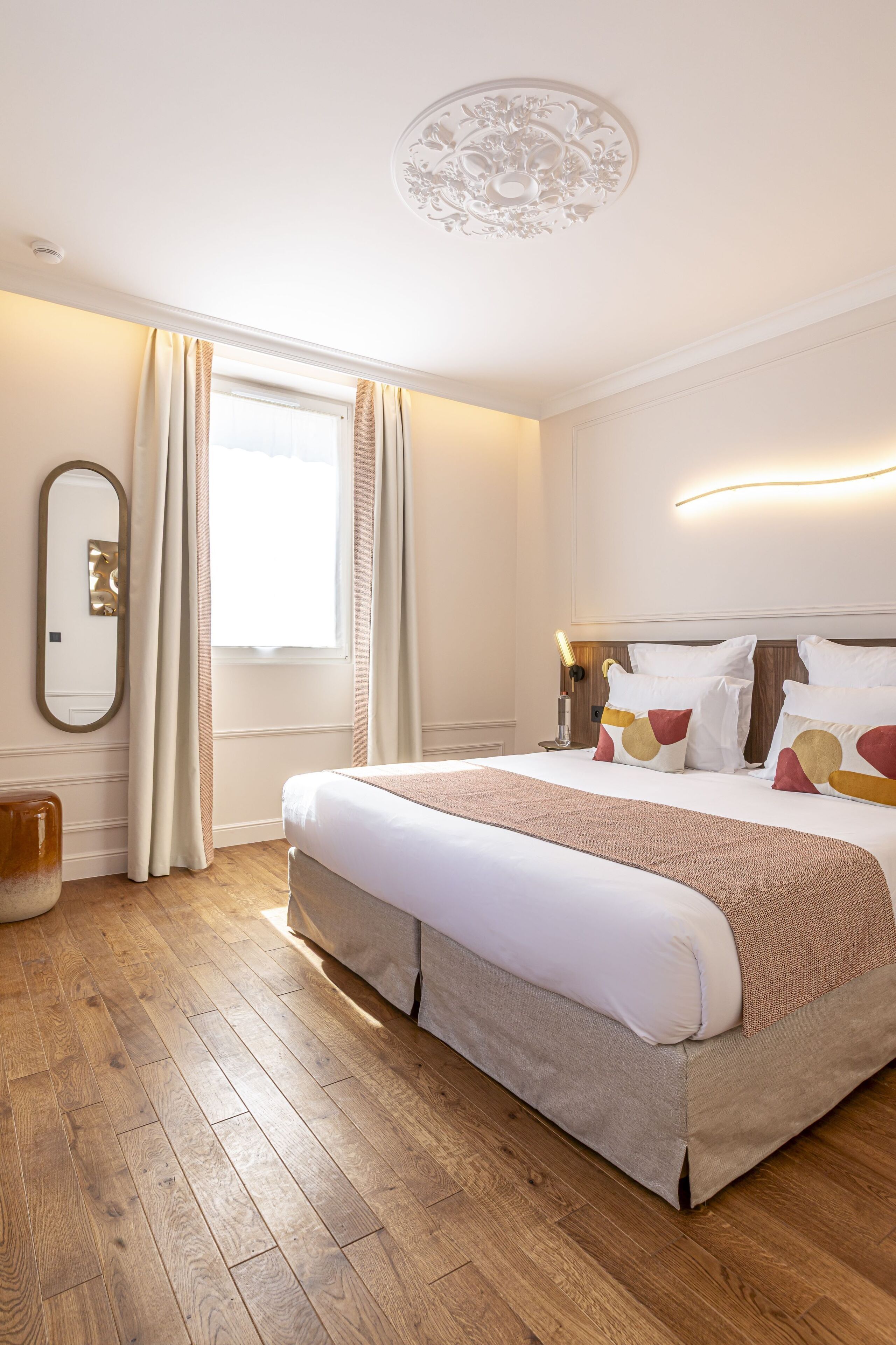 A neatly arranged hotel room with a large bed, a bedside table, a mirror, and a window with curtains.