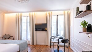 Una habitación de hotel con cama, televisión, mesa de comedor con sillas y ventana con cortinas.