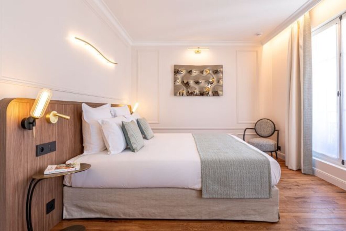 A modern hotel room with a large bed, bedside lamps, a small table, and a chair.