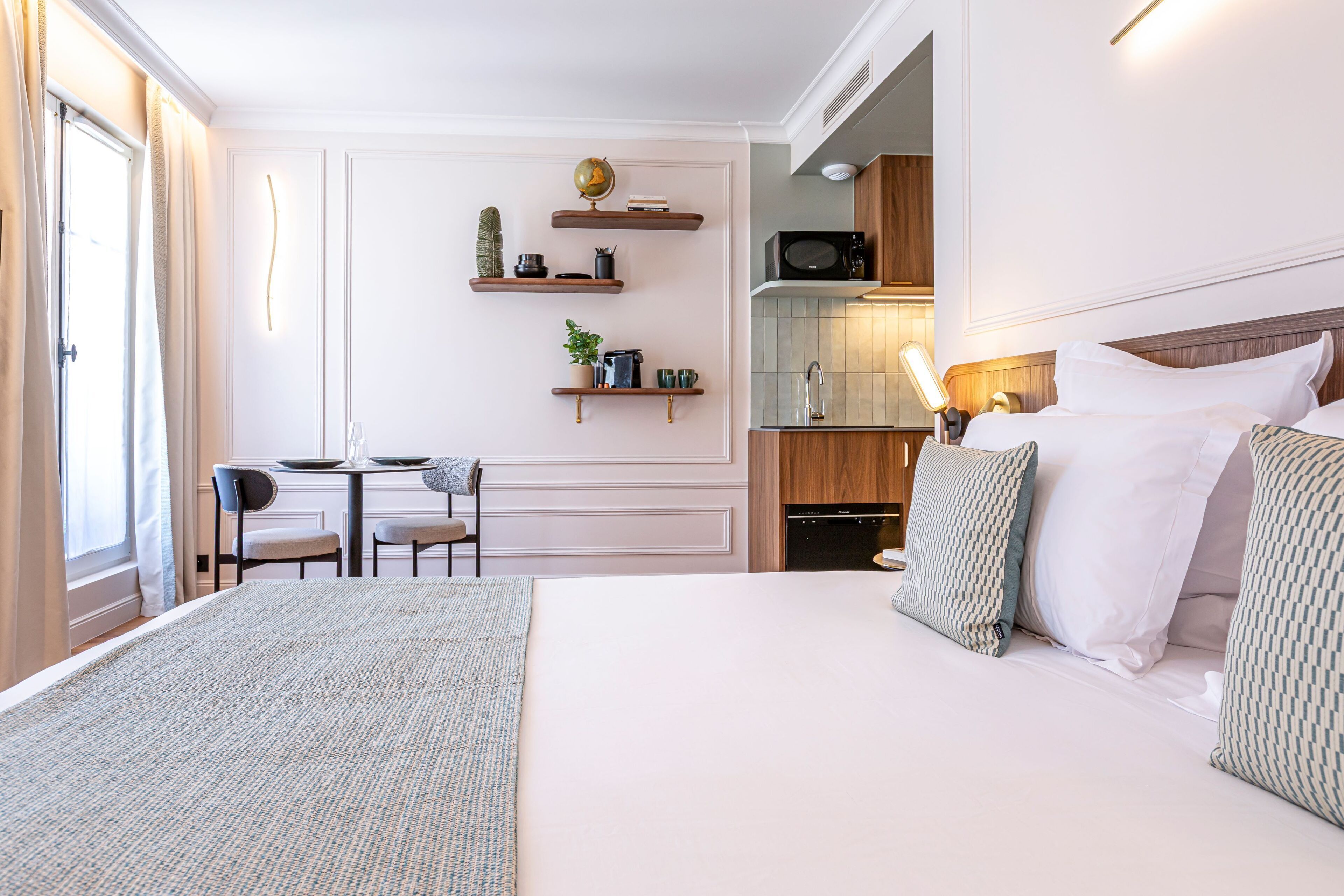 Quarto de hotel com uma cama grande, uma escrivaninha com cadeiras, uma cozinha compacta e um banheiro.