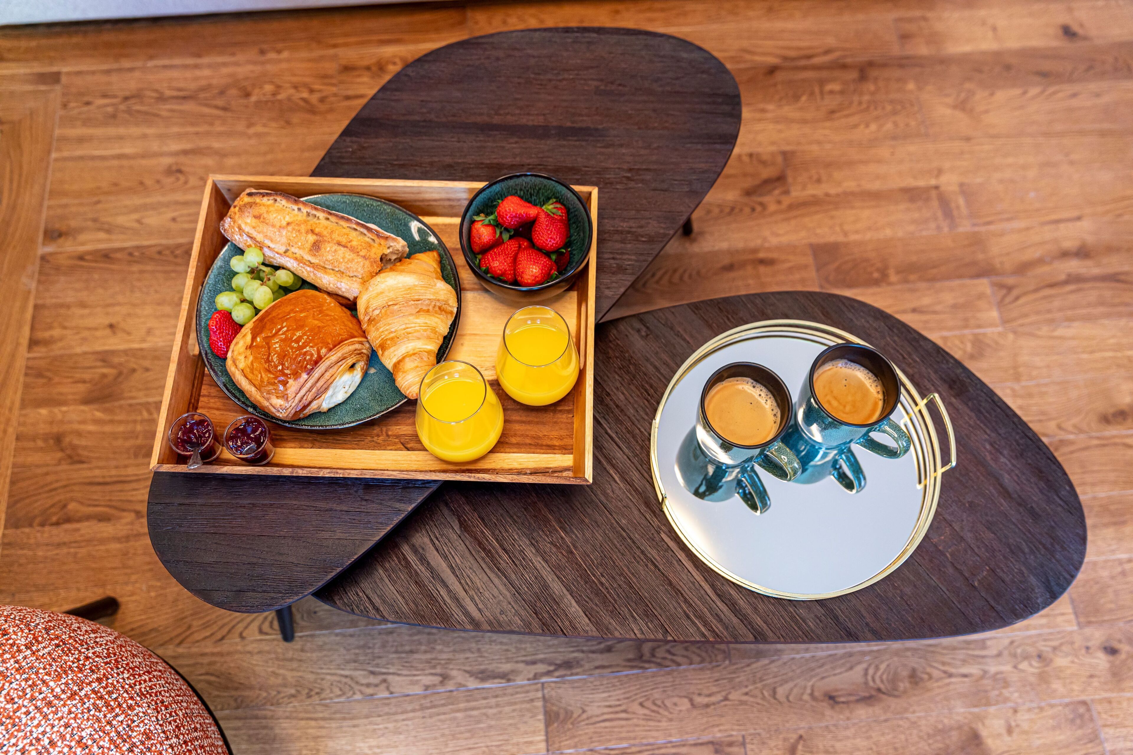 A breakfast tray with croissants, strawberries, grapes, and orange juice on a wooden table.