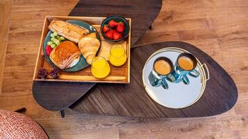 A breakfast tray with croissants, strawberries, grapes, and orange juice on a wooden table.