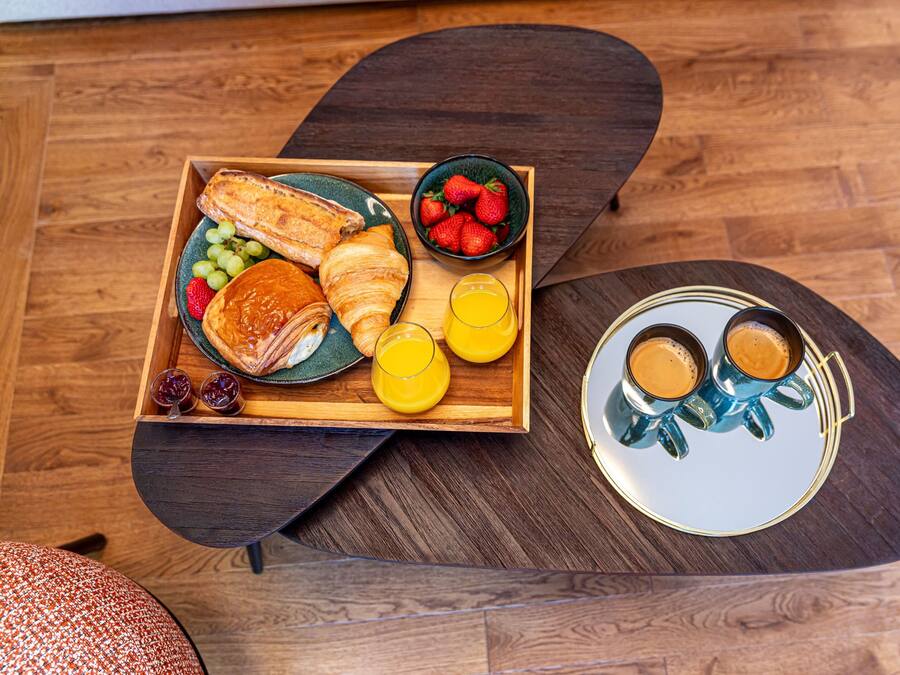 A breakfast tray with croissants, strawberries, grapes, and orange juice on a wooden table.