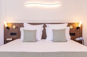 A hotel room with a large bed, two bedside tables, a wall-mounted light fixture, and a small round table with a lamp. - Villa SoPi Appart'Hotel by Patrick Hayat (Paris)