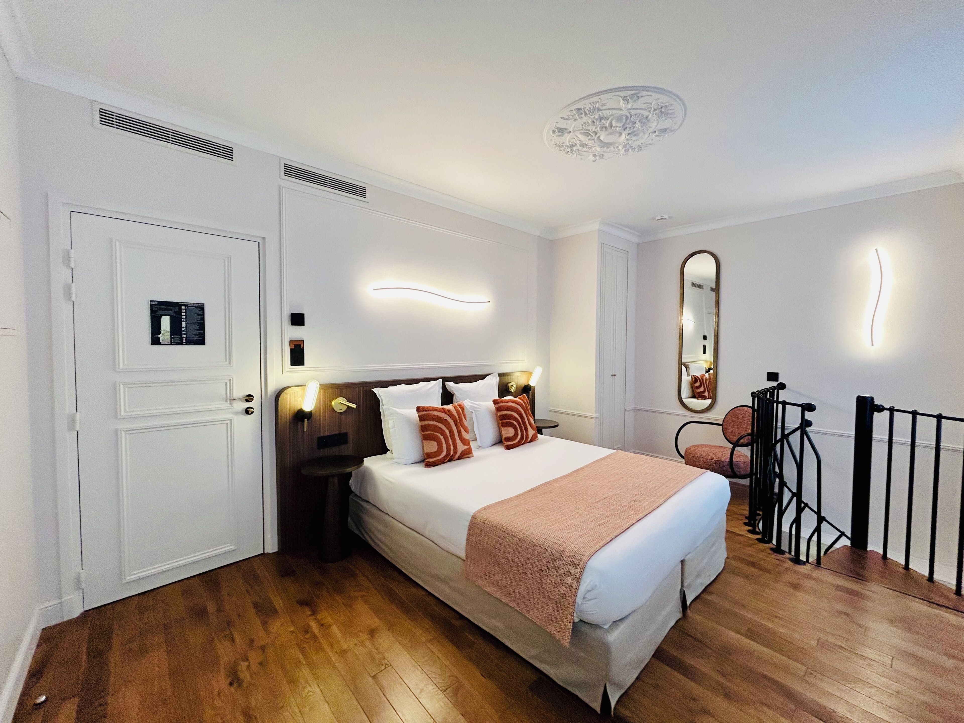A hotel room with a large bed, bedside tables, a mirror, and a wooden floor.