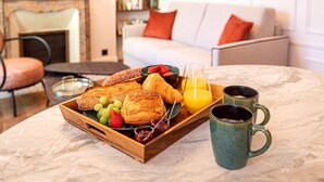 Una bandeja de desayuno con croissants, fresas y jugo sobre una mesa de mármol en una sala de estar con un sofá y una chimenea al fondo.