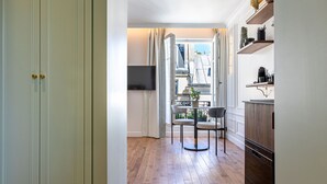 Un pasillo con suelo de madera, un comedor con sillas y una mesa, y una cocina con estantes y armarios.