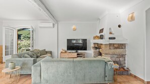 A modern living room with a sectional sofa, a flat-screen TV, a stone fireplace, and a view of the outdoors. - Vacation home, 250 m from the beach (Théoule-sur-Mer)