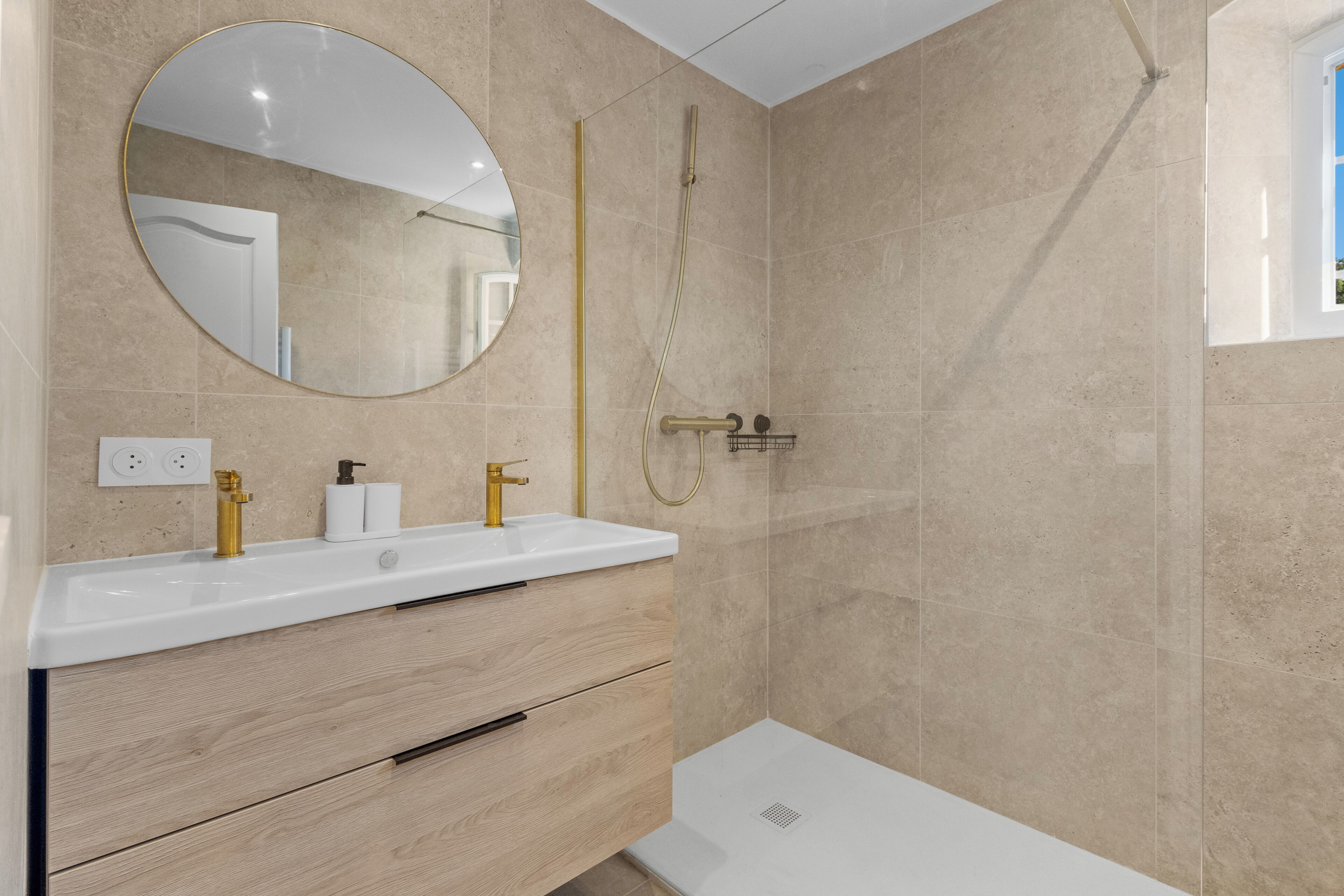 A modern bathroom with a white sink, gold fixtures, a large mirror, and beige tiled walls.