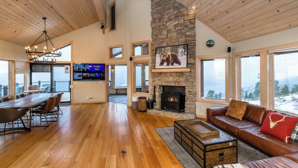 A spacious living area with a stone fireplace, wooden floors, a leather sofa, and a dining table with chairs. - MilkyWay_Lake Views! Air Conditioning, 3850SqFt, 3 Story, Game Room + HOA Amenities (Truckee)