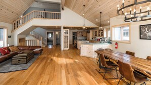 A spacious living area with a wooden floor, a dining table, and a loft with a staircase. - MilkyWay_Lake Views! Air Conditioning, 3850SqFt, 3 Story, Game Room + HOA Amenities (Truckee)