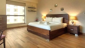 A hotel room with a large bed, wooden flooring, a desk, and a window with a view of buildings. - JBR Rimal 1 Spacious 3BR close to Beach (Dubai)