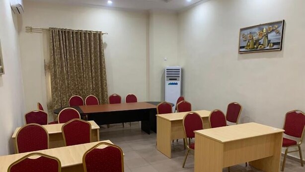 A conference room with a long table, red chairs, and a painting on the wall. - Suitoria Hotels  (Ilorin)