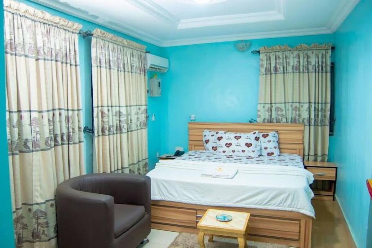 A bedroom with a bed, a chair, a bedside table, and curtains.