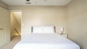 Une chambre à coucher comprenant un lit, une table de chevet, un ventilateur de plafond et une porte donnant sur une autre pièce.