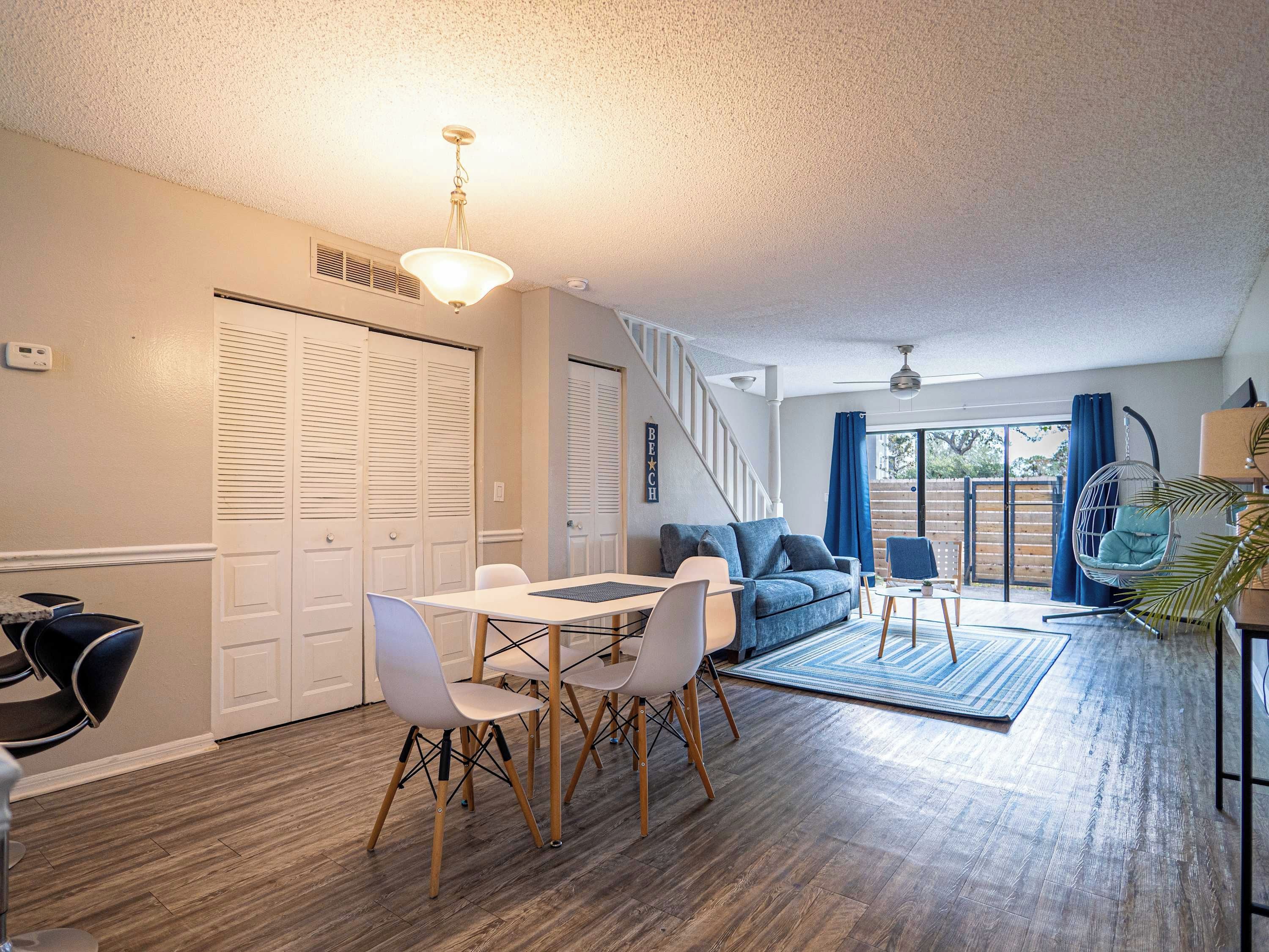 A spacious living area with a dining table, chairs, a sofa, and a hanging chair. There are sliding doors and a view of the outdoors.