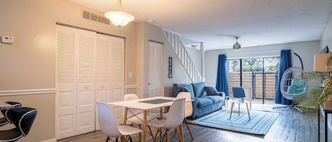 A spacious living area with a dining table, chairs, a sofa, and a hanging chair. There are sliding doors and a view of the outdoors.