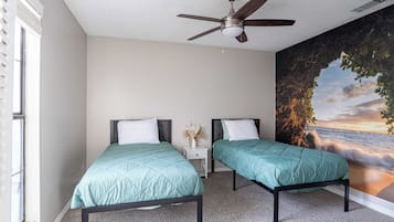 A bedroom with two beds, a ceiling fan, a nightstand, and a large mural of a sunset over the ocean.