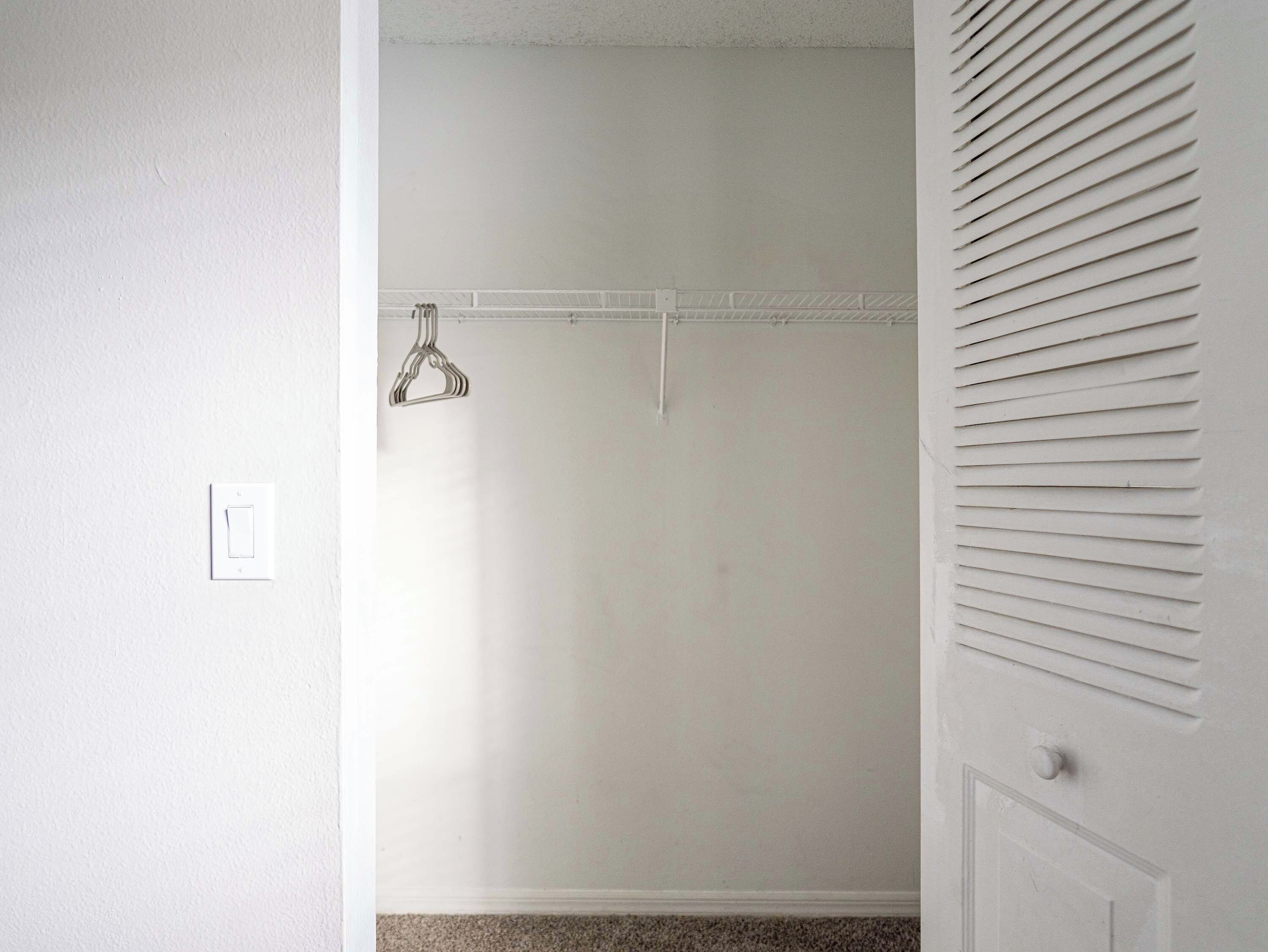 A room with a white door, a white wall, and a white ceiling. There is a white ceiling vent on the right side of the image.