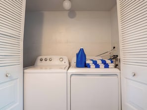 Un lavadero con lavadora y secadora Whirlpool, una botella de detergente azul y una toalla doblada en azul y blanco.