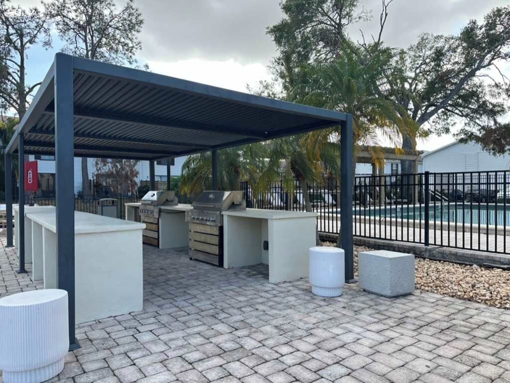 An outdoor patio with a grill and seating area, surrounded by a fence and trees.