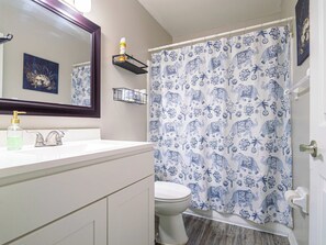 Une salle de bain avec un lavabo blanc, un miroir, des toilettes et un rideau de douche orné de motifs d’éléphants.