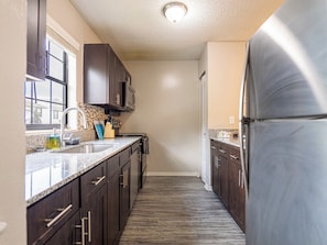 Una cocina estrecha con armarios de madera oscura, un refrigerador de acero inoxidable y una encimera de granito.