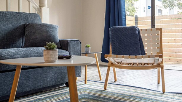 Ein modernes Wohnzimmer mit grauem Sofa, einem Holzstuhl, einem kleinen Tisch und einer Topfpflanze.