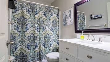 Une salle de bain avec un rideau de douche à motifs, des toilettes, un lavabo avec un miroir et un flacon de savon pour les mains.