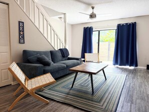 Ein Wohnzimmer mit einer Couch, einem Holzstuhl, einem Couchtisch, einem Teppich und einer Treppe.