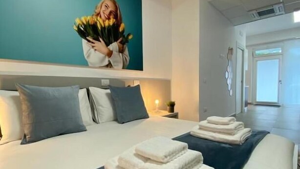 A modern hotel room with a large bed, a teal accent wall, and a picture of a woman holding flowers. - BEEAPARTMENTS  (Bari)
