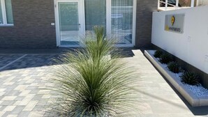 A modern building with a glass door entrance, a potted plant in the foreground, and a white wall with a logo. - BEEAPARTMENTS  (Bari)