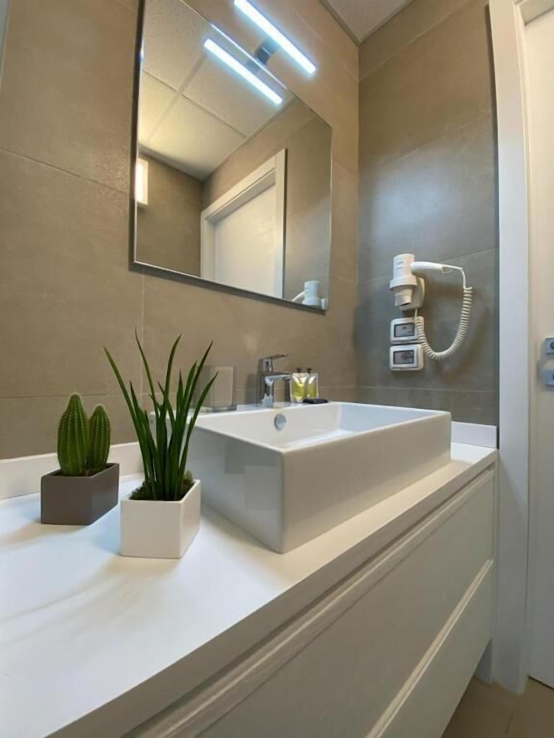 A modern bathroom with a large rectangular sink, a mirror, and a telephone. There are two potted plants on the vanity.