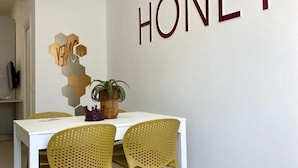 A dining area with a white table and yellow chairs, a wall-mounted sign reading "HONEY", and a decorative hexagonal piece on the wall. - BEEAPARTMENTS  (Bari)