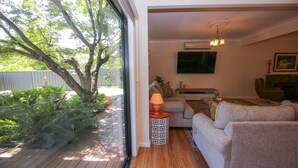 A living room with a sofa, a coffee table, and a lamp. There is a TV mounted on the wall and a fireplace in the background.
